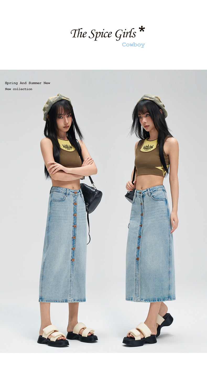 Two female models wearing matching outfits consisting of olive green crop tops with yellow graphic prints and light blue denim midi skirt button-downs, standing against a light gray studio background. The top has text 'The Spice Girls' and 'Coworkry' visible.