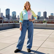 Woman wearing a colorful shirt and blue jeans on a rooftop with city skyline in the background