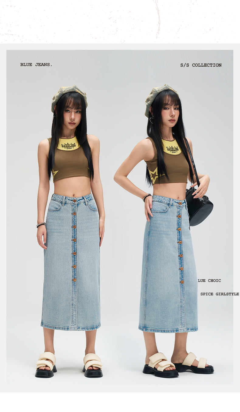 Two female models standing side by side in a studio setting, wearing matching outfits consisting of olive green crop tops with gold star details and light blue denim midi skirts with front buttons. The left model wears beige sandals, and the right model wears black sandals and carries a black shoulder bag.