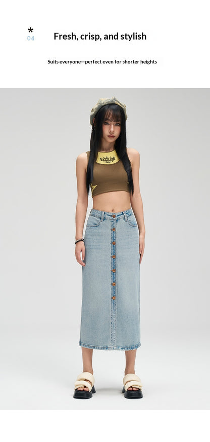 A model stands against a light gray studio background wearing a light-wash denim midi skirt with front buttons, a brown cropped tank top, beige sandals, and a gold necklace. Text at the top reads 'Fresh, crisp, and stylish' and 'Suits everyone—perfect even for shorter heights.