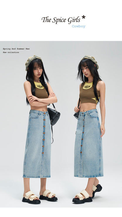 Two female models wearing matching outfits consisting of olive green crop tops with yellow graphic prints and light blue denim midi skirt button-downs, standing against a light gray studio background. The top has text 'The Spice Girls' and 'Coworkry' visible.