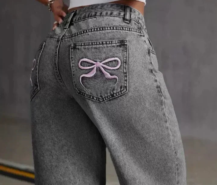 Gray jeans with a decorative bow patch on the back pocket against a gray background
