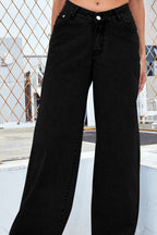 Person wearing black wide-leg jeans standing on a rooftop with a geometric metal fence in the background.