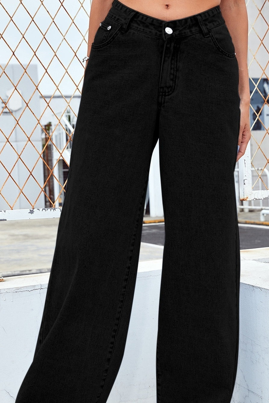 Person wearing black wide-leg jeans standing on a rooftop with a geometric metal fence in the background.