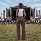 Person standing on a grassy field facing a music festival stage with colorful banners.