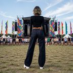 Person standing in a field at a music festival with colorful flags and stage in the background