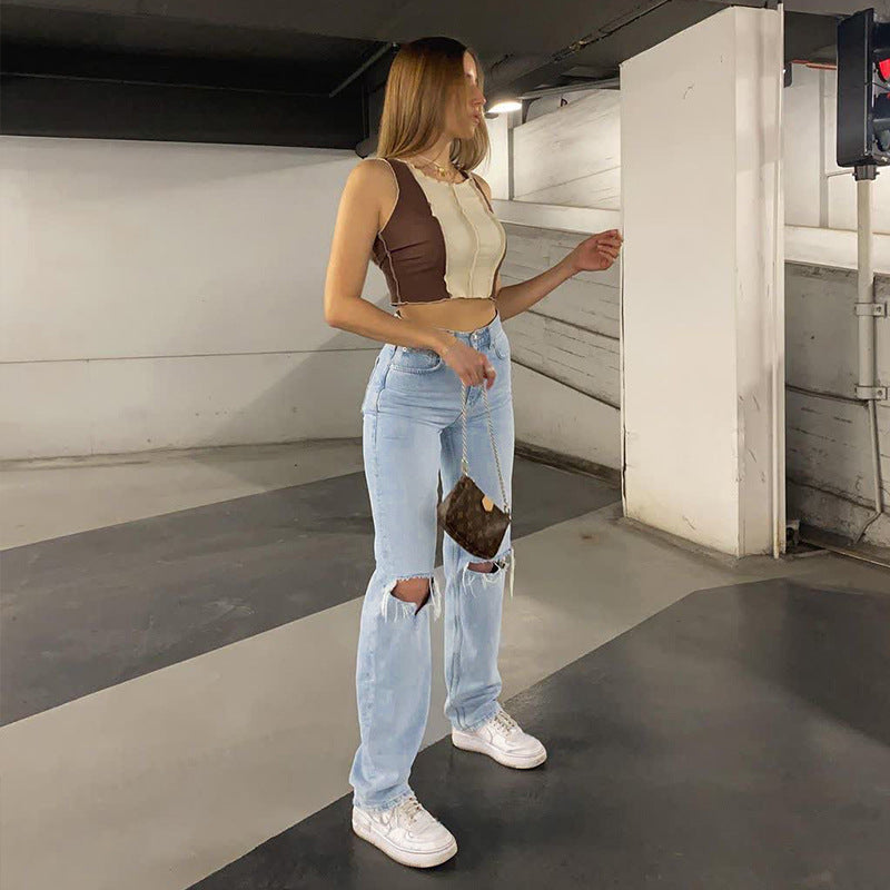 Woman in a parking garage wearing a crop top, jeans, and white sneakers.