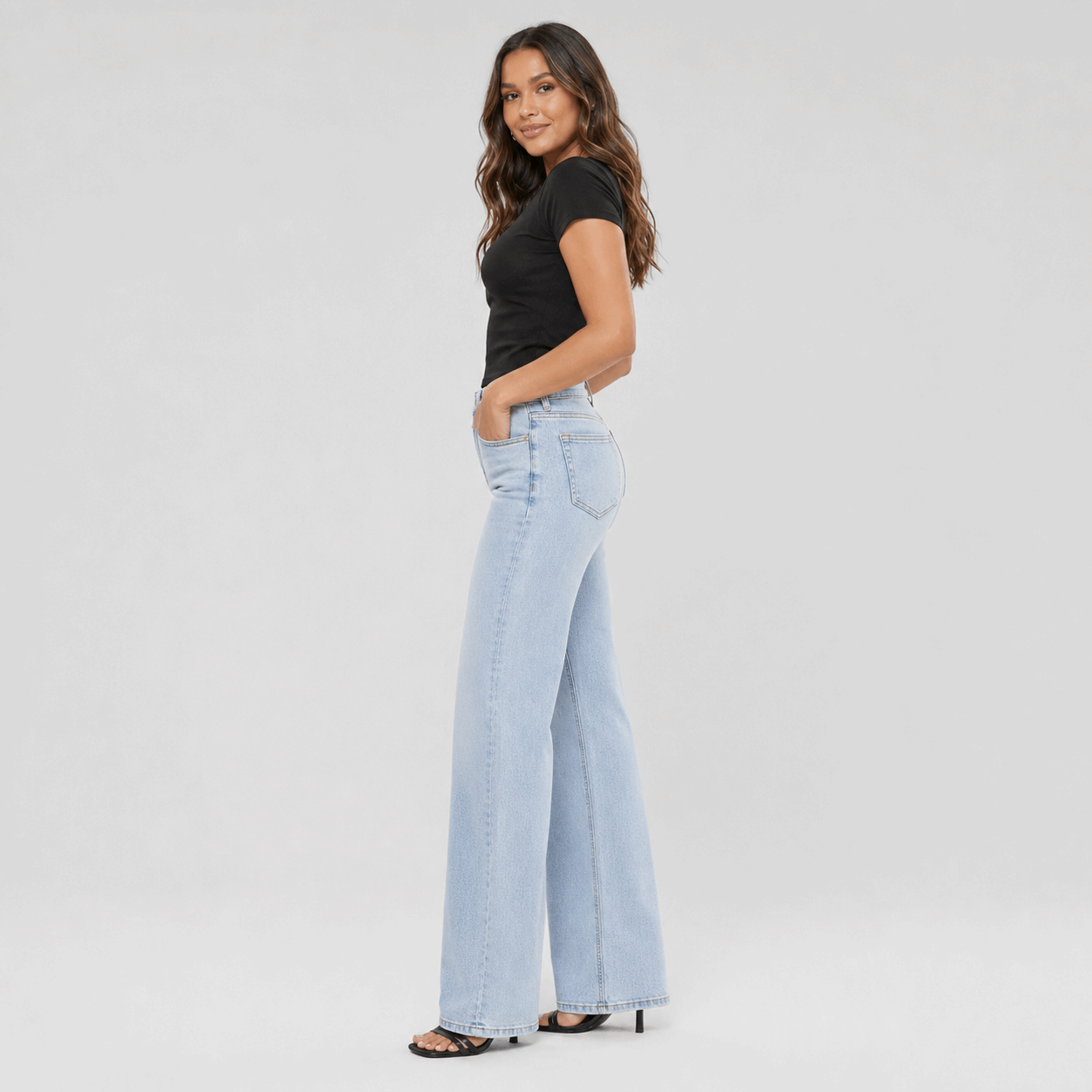 Woman wearing light blue flared jeans and a black top on a white background