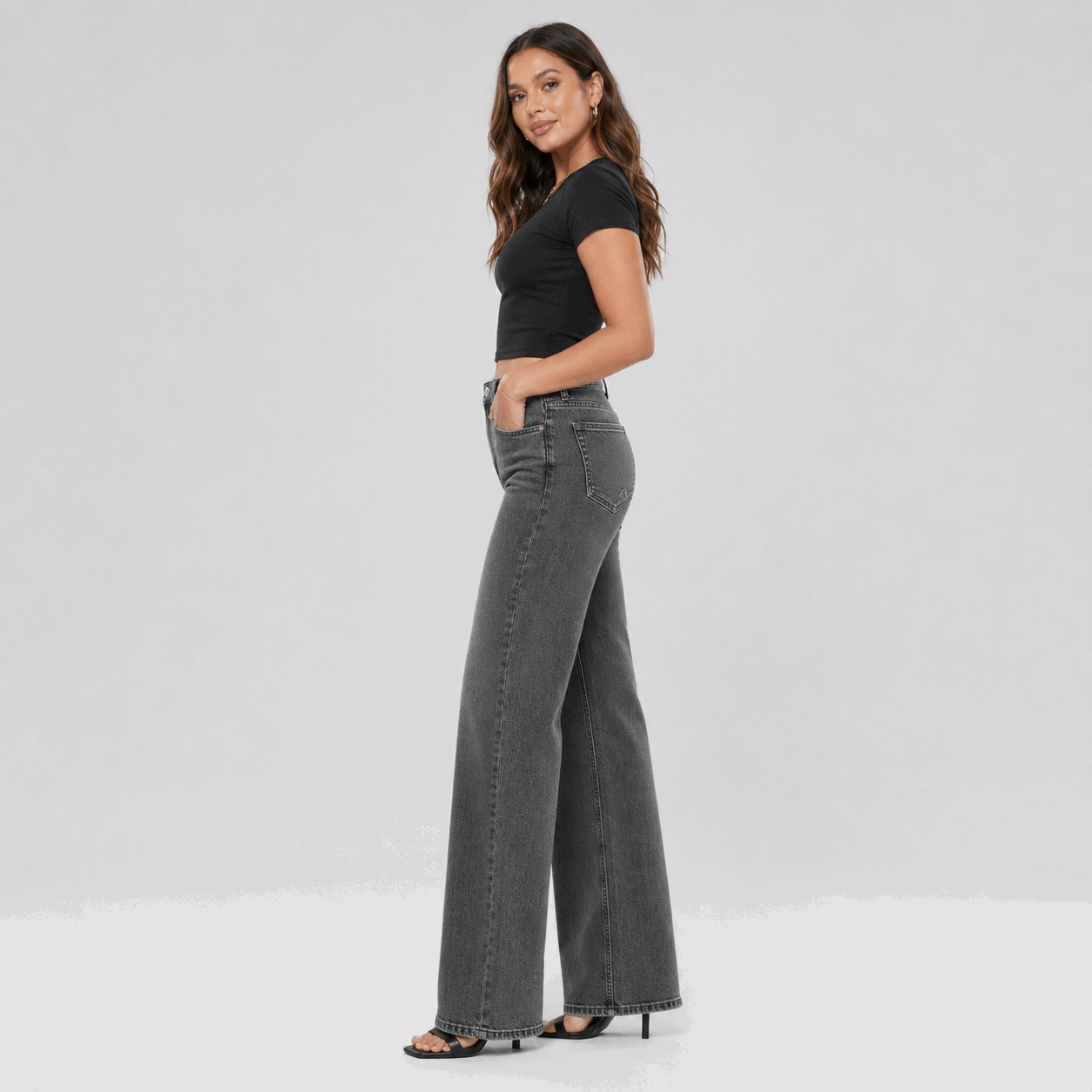 Woman wearing gray wide-leg jeans and a black top on a light gray background