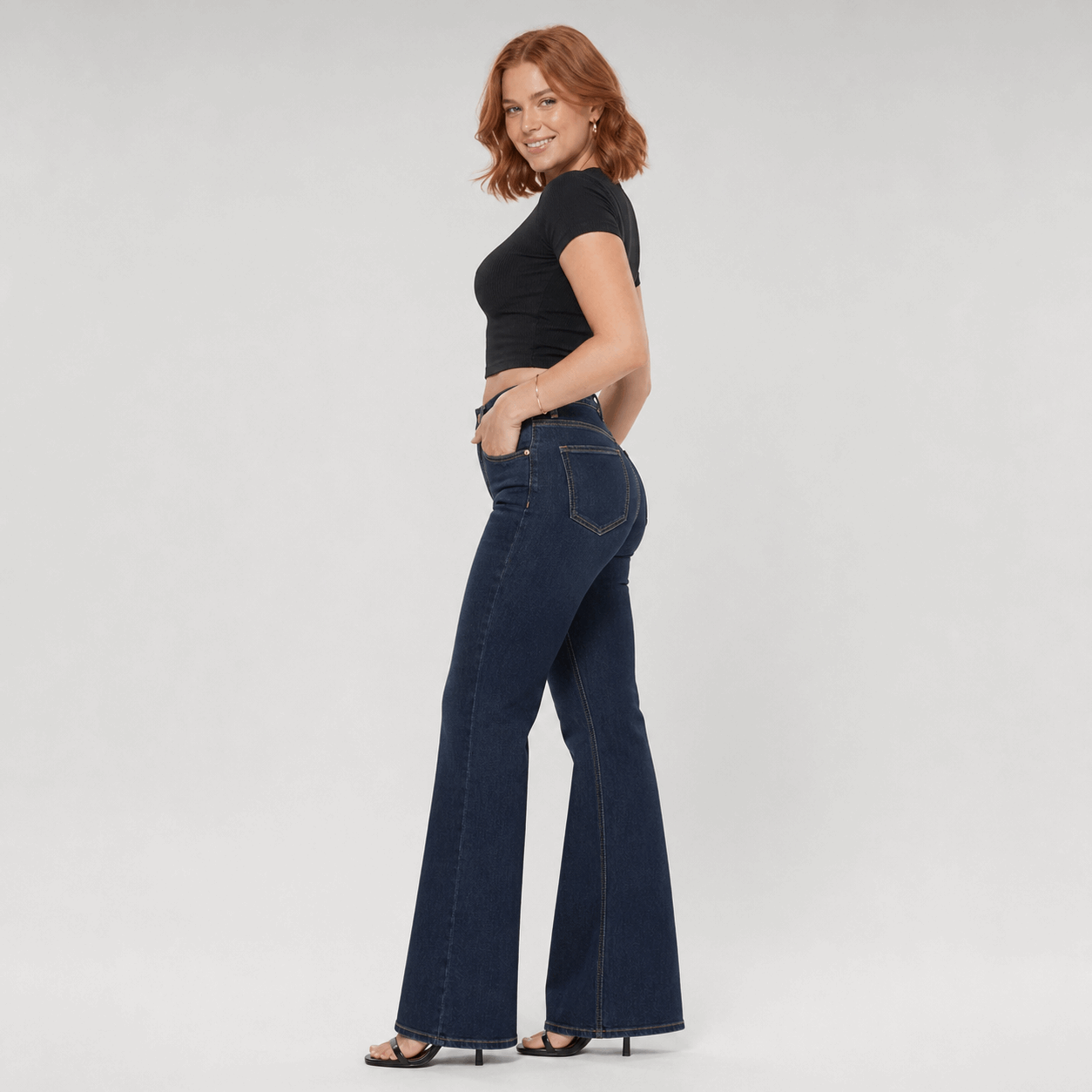Woman wearing dark blue flared jeans and a black top on a light gray background