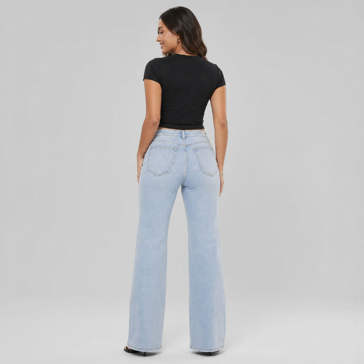 Woman wearing light blue jeans and a black top on a gray background