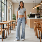 A woman stands in a modern cafe wearing a light gray short-sleeve crop top and light-wash wide-leg jeans, paired with white slip-on shoes.