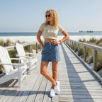 Woman standing on a wooden boardwalk by the beach wearing a striped crop top and denim skirt.